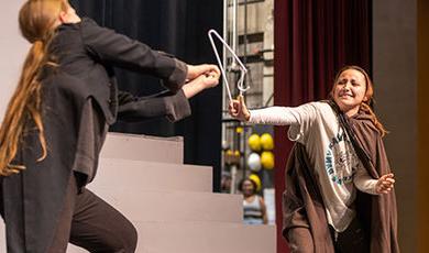 Two students rehearse a scene using a broken hanger as a prop.